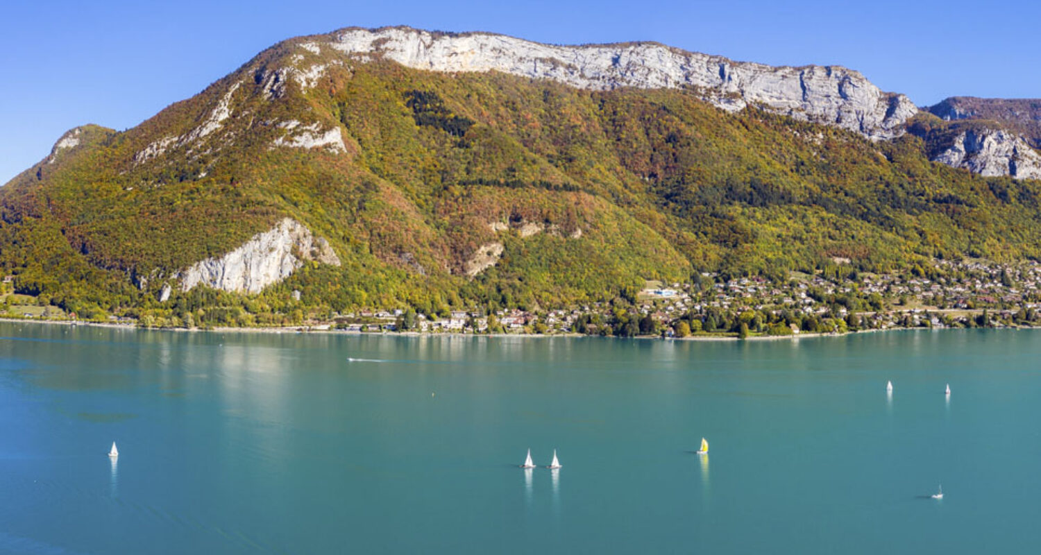 Lac d’Annecy entouré de reliefs montagneux verdoyants.